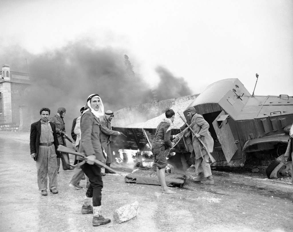 Arab snipers move away from a flaming Jewish truck in the Sheik Jarrah quarter of Jerusalem after dragging the body of driver from armored cab and dumping it on the road on March 7, 1948. The truck was caught in sniper fire, crashed into a wall and burst into flames. Ref #: PA.2539510  Date: 07/03/1948