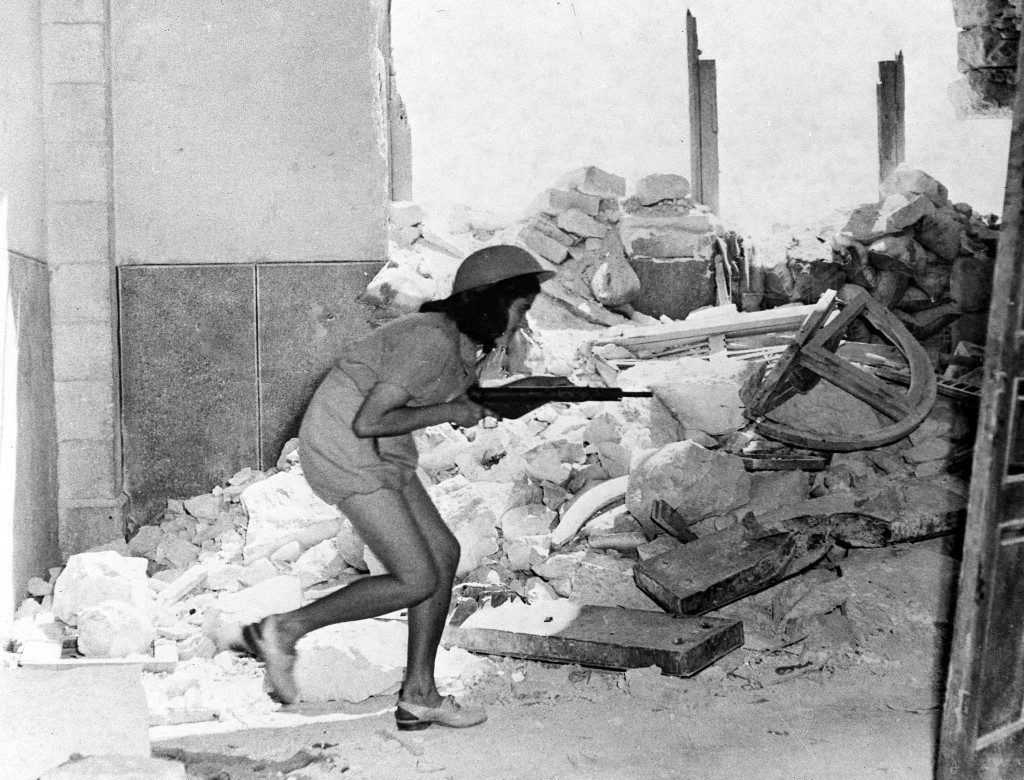 An Israeli soldier, armed with a sten gun, picks her way through the shattered walls of Sulimans Way, in the old city of Jerusalem, Palestine, July 20, 1948, which forms a front line between the Arabs inside and Jewish forces outside the walls. Fierce fighting happened between the two forces following the expiry of a two-day truce. (AP Photo/Pringle) Ref #: PA.5736824  Date: 20/07/1948 