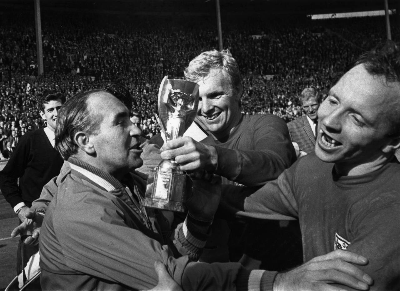 England Manager Alf Ramsey (left) celebrates his team's 4-2 victory in extra time over West Germany in the World Cup Final at Wembley Stadium. With him is captain Bobby Moore (1941 - 1993), holding the Jules Rimet Trophy, and team mate Nobby Stiles, 30th July 1966. (Photo by Hulton Archive/Getty Images)