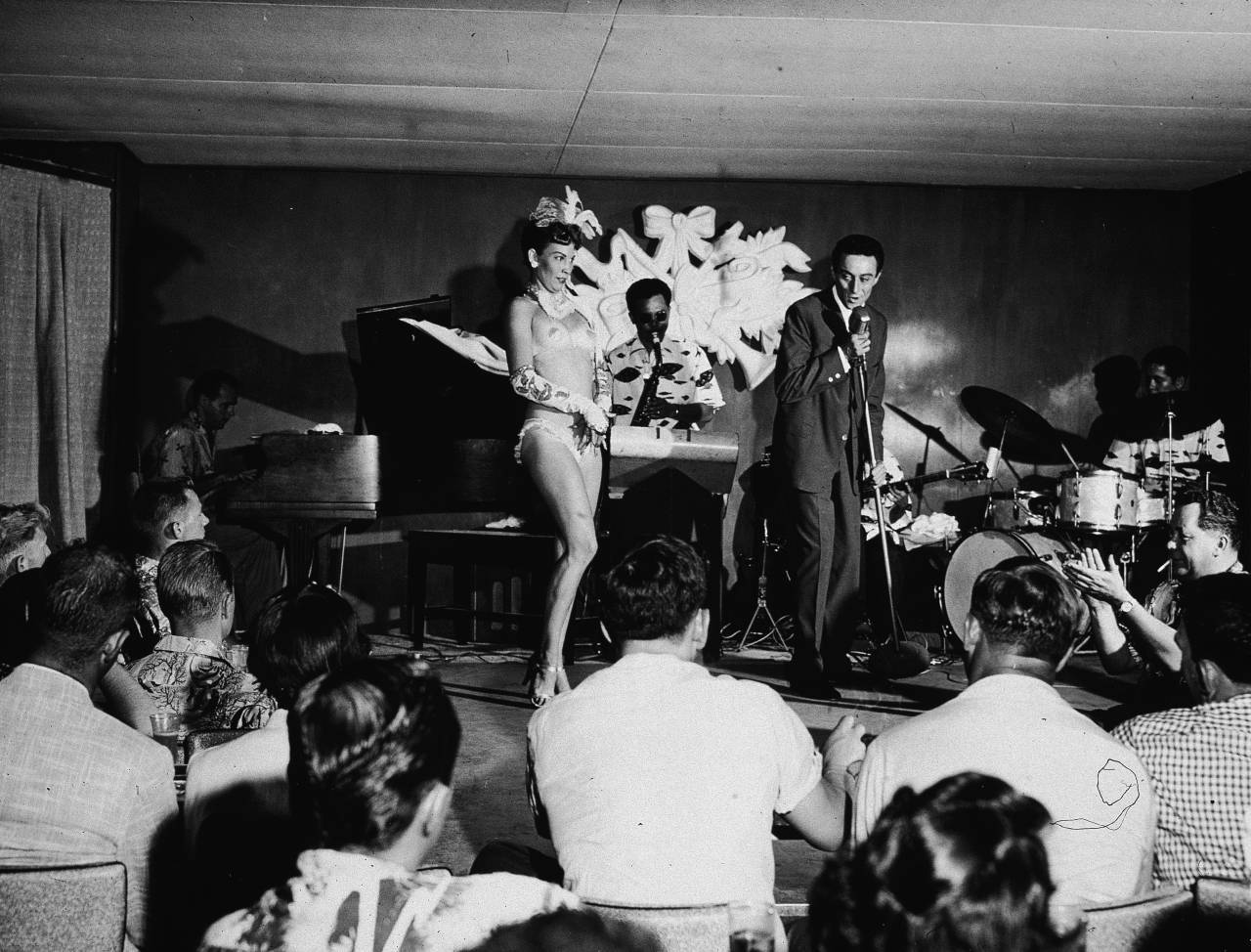 American comedian Lenny Bruce (1926 - 1966) performs on stage with exotic dancer Windee Gayle and a saxophonist at the Orchid Room, Waikiki, 1950s. (Photo by Hulton Archive/Getty Images)