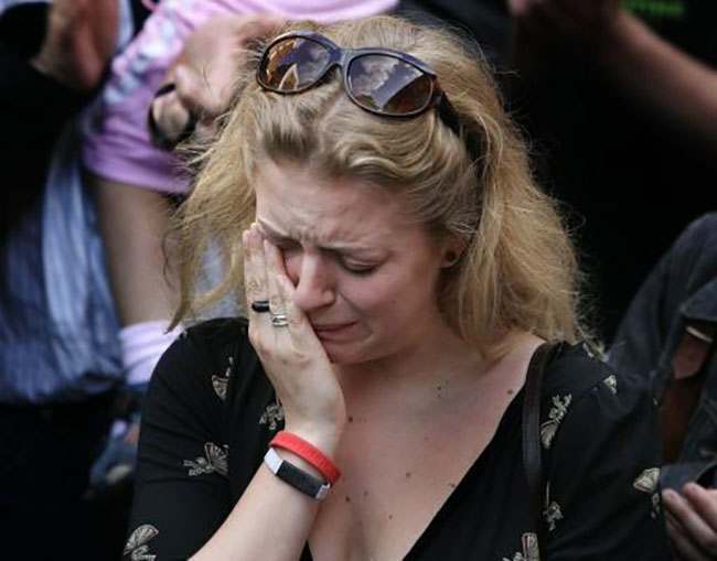 A woman wipes away tears as she observes a moment of silence in remembrance of the victims of Thursday's London bombings, during a memorial in a park near King's Cross station in central London, Saturday July 9, 2005. Police revised the timing of the deadly blasts that tore through the London Underground, saying on Saturday the explosions were detonated just seconds apart and were so powerful that none of the 49 dead have been identified and bodies remain trapped deep inside a subway tunnel. Hundreds have been reported missing. (AP Photo/Lefteris Pitarakis)