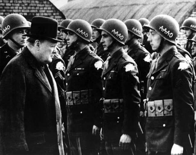 British Prime Minister Winston Churchill, left, reviews American troops at a base in England on the eve of D-Day, June 1944, during World War II. The initials AAAO on the steel helmets with a line across the As stands for "Anywhere, Anytime, Anyhow, Bar Nothing." The identification shoulder patches of the G.I.s are blotted out by the censor. (AP Photo)