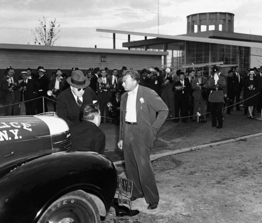 Fair bombing explained to LaGuardia detective Fred Morelock, right, explains to Mayor F. H. LaGuardia, seated on auto bumper, and police commissioner Lewis J. Valentine, left, how he removed a time bomb from the British pavilion at the New York worlds fair on July 4, 1940 after it had been found by an attendant. After the bomb had been removed to the rear of the polish pavilion and detectives were examining it. The bomb exploded, killing two and injuring five. 