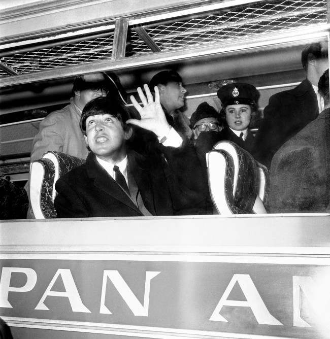 Paul McCartney looks up and acknowledges the waves and screams shortly after arriving with the other three Beatles at London Airport from America.