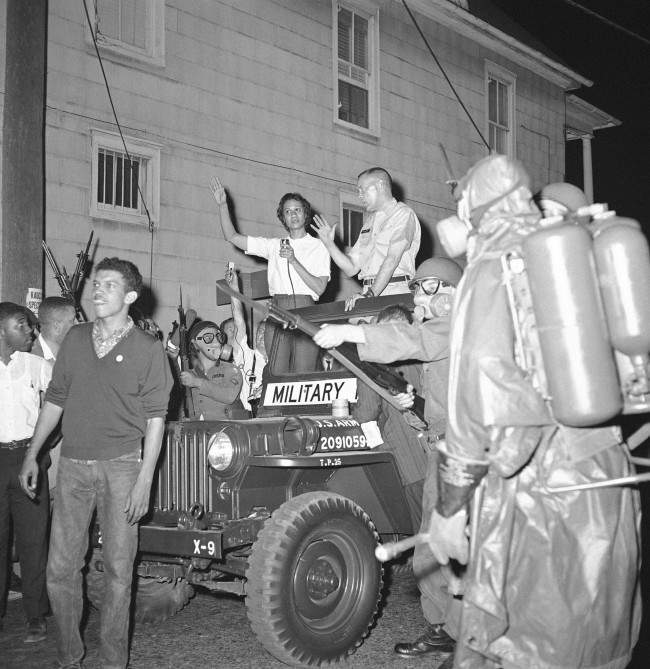 Masked National Guardsman with their bayonets held at the ready surround the jeep of Brig. Gen. George Gelson, head of the guard unit, as Stanley Branche, chairman of the Committee for Freedom Now, left, and Mrs. Gloria Richardson, left, stands beside him in Cambridge, Maryland on May 11, 1964. The guard had to disperse a crowd of approximately 300 who tried to march toward the arena where Alabama Gov. George Wallace was speaking.