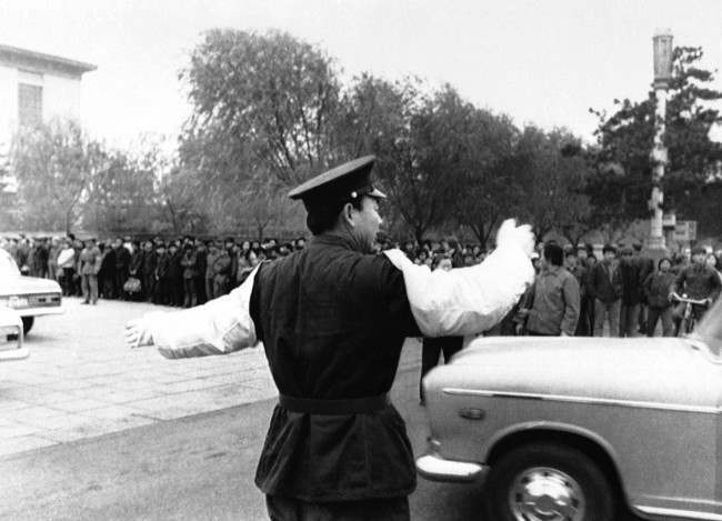 A policeman directs the official cars arriving for the opening of the trial of Gang of Four in the Ministry of Public Security in Peking on Thursday, Nov. 20, 1980. More than a thousand bystanders watch the arrival of the motorcade as foreign press are not allowed inside the courtroom. 