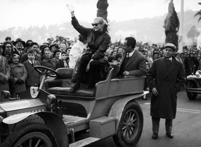Swedish-born actress Anita Ekberg, warmly dressed like the spectators on a cool day, waves from the top of a 1906 model automobile (Digion Bouton) with which she took part in a motorized carnival cortege in Rapallo, Italy on Feb. 8, 1959. Miss Ekberg, who is the wife of British actor Anthony Steel, is in Italy studying the script of her part in star director Federico Fellini (La Strada) new movie ÂLa Dolce VitaÂ (The Sweet Life). (AP Photo/Gino Calza)