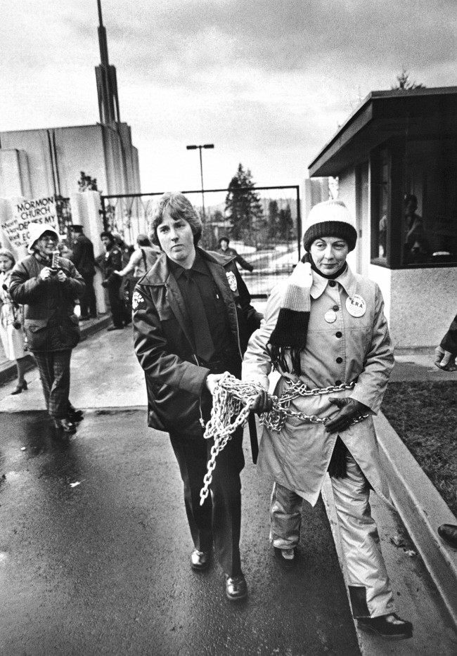 Sonia Johnson is led away from the gate of a new $12 million Morman temple by a police officer after she had chained herself to the gate during a pro-Equal Rights Amendment demonstration in Bellevue, Washington on Nov. 17, 1980. Johnson was excommunicated from the Church of Jesus Christ of Latter-Day Saints about a year ago after publicly speaking in favor of the ERA. 