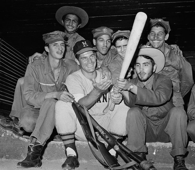 A rebel solider from the Fidel Castro army gets a kick out of trying the bat of Charley Lau, Detroit catcher, playing ball in the Cuban winter league, February 1, 1959. Lau made the boys let him keep their guns so he would be sure and get his favorite stick back.