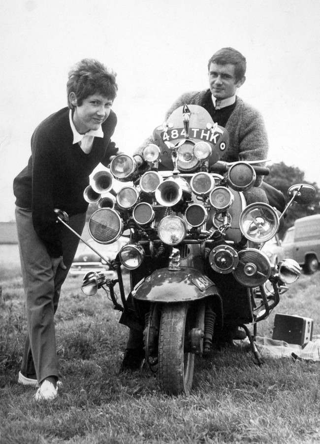 The modern fad for having as much sound and light as possible on your scooter reached the Epsom Downs for Derby Day. Proud owners of this laden-down Vespa scooter are Roy Young and Linda Jarvis. Date: 31/05/1964 