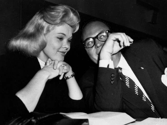 Burlesque dancer Candy Barr, left, smiles prettily as her attorney, Lester May, whispers to her at the defense table at the opening of her trial, Feb. 10, 1958, Dallas, Texas. The dancer is charged with illegal possession of narcotics