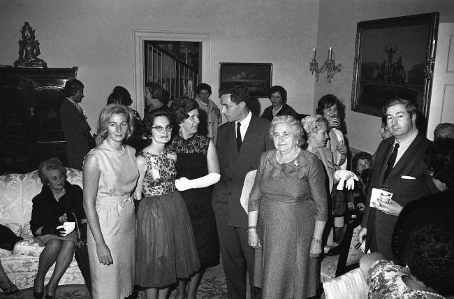 Rhode Islanders attending the campaign conference of democratic Women in Washington on May 1, 1964 were guests of Sen. and Mrs. Claiborne Pell, D-R.I., at their home in the capital. What had been planned as a garden party had to be held indoors because of the week-long rains. Group from left: Mrs. Nuala Pell; Mrs. Anne McGeough, Mrs. Constance Savard, Sen.Claiborne Pell and Mrs. Kathleen McDonald. Mrs. Pell is wearing light colored sleeveless dress standing at left of group. 