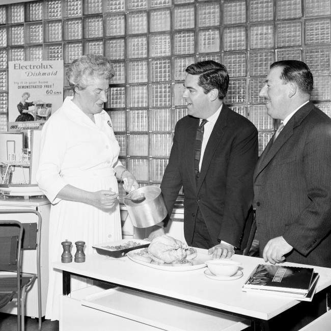 Mr Robert Carrier (centre) gourmet and food writer, watches Miss Mary Barnard, a senior demonstrator of the London electricity Board, prepare a meal of boiled chicken, vegetables and sauces at the boards showroom in Regent Street, London, today. Date: 01/03/1963 