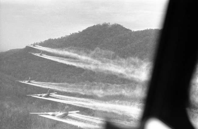 Flying a bare 100 feet above the jungle hills west of Hue, 5 bulky C-123 ?providers? cut loose with a spray of chemical defoliant on August 14, 1968. The planes are flown by U.S. air force crews who have nicknamed themselves the ?ranch hands?. The chemicals used burn off heavy foliage hiding enemy infiltrations routes and base camps. So far in Vietnam more than 4 million acres have been sprayed with the defoliant and plans call for new target areas to match the increased infiltration of North Vietnamese in to the south. The aircraft are specially equipped with huge 1,000 gallon tanks holding 11,000 lbs. of herbicide. To hit their target areas they fly barely above the tree tops and in tight formation. In particularly dangerous areas they are provided with fighter-bomber escorts. 
