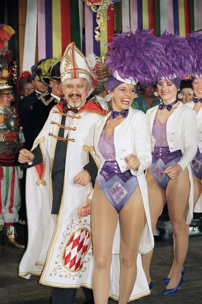 German government spokesman Hans Klein, dressed in carnival costume, left, smiles surrounded by dancers at a carnival party on February 21, 1990 at the Chancellery in Bonn, Germany.