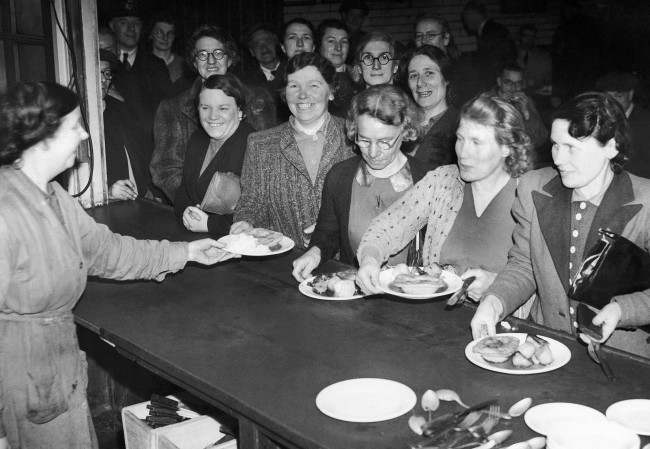 Nearly half of the post office staff consists of women now that the men are being absorbed into the forces. In their own training school they learn everything connected with the collection and delivery of the mail. A meal from the canteen forms a welcome lunch-time break after concentrated studies on Feb. 16, 1942.