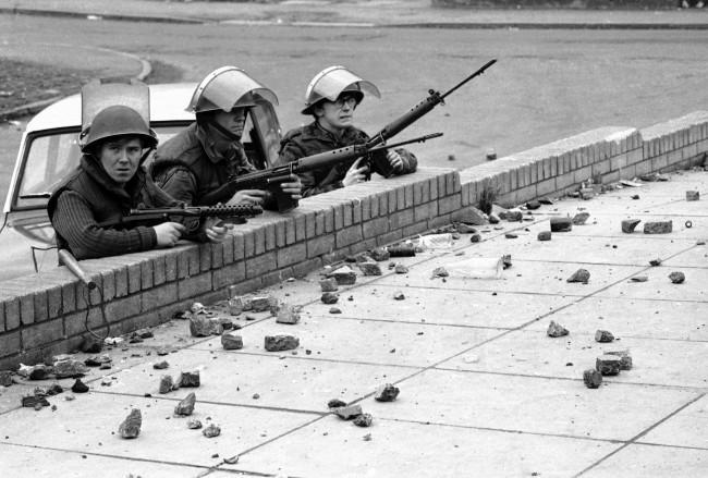 Three British soldiers, two armed with automatic rifles, and man at left with a Stirling sub-machinegun, shelter behind a wall in the Andersonstown area of Belfast, Northern Ireland on Nov. 1, 1971, during riots which followed the shooting of two policemen. (AP Photo/Peter Kemp)