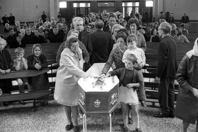 Mourners file past the coffin of Father Hugh Mullan, at Corpus Christi Roman Catholic Church on the Ballymurphy estate after Requiem Mass. Father Hugh, 37, was killed during Monday night's bloodbath in Belfast, which occurred after the announcement of internment of terrorists, after attempting to give last rites to a wounded parishioner. He was curate of St John's in Falls Road and he will be buried in his home town of Portaferry in County Down, Northern Ireland. Date: 11/08/1971