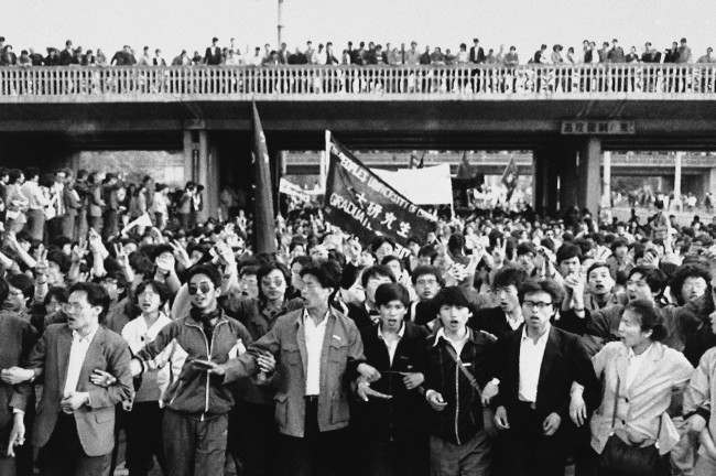 Jubilant student marchers, arms lined, pass under a bridge lined with local supporters, Thursday, April 27, 1989, Beijing, China. Students in the ten of thousands from several Beijing schools demonstrated in defiance of a government ban. (AP Photo/Mark Avery)