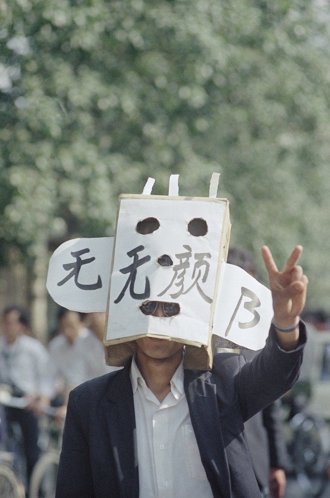 A student protestor flashes a victory sign during a demonstration in Tiananmen Square, Wednesday, May 17, 1989, Beijing, China. The characters on his mask mean losing face. (AP Photo/Mark Avery)