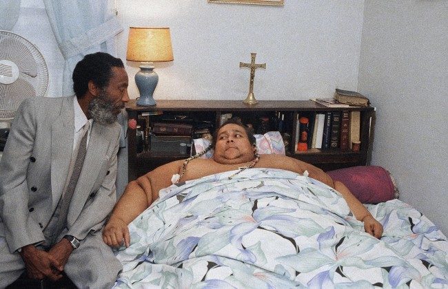 Walter Hudson, who is heavier than the heaviest man listed by the Guinness Book of World Records, listens as Dick Gregory talks with him at his home in Hempstead, New York, Oct. 7, 1987