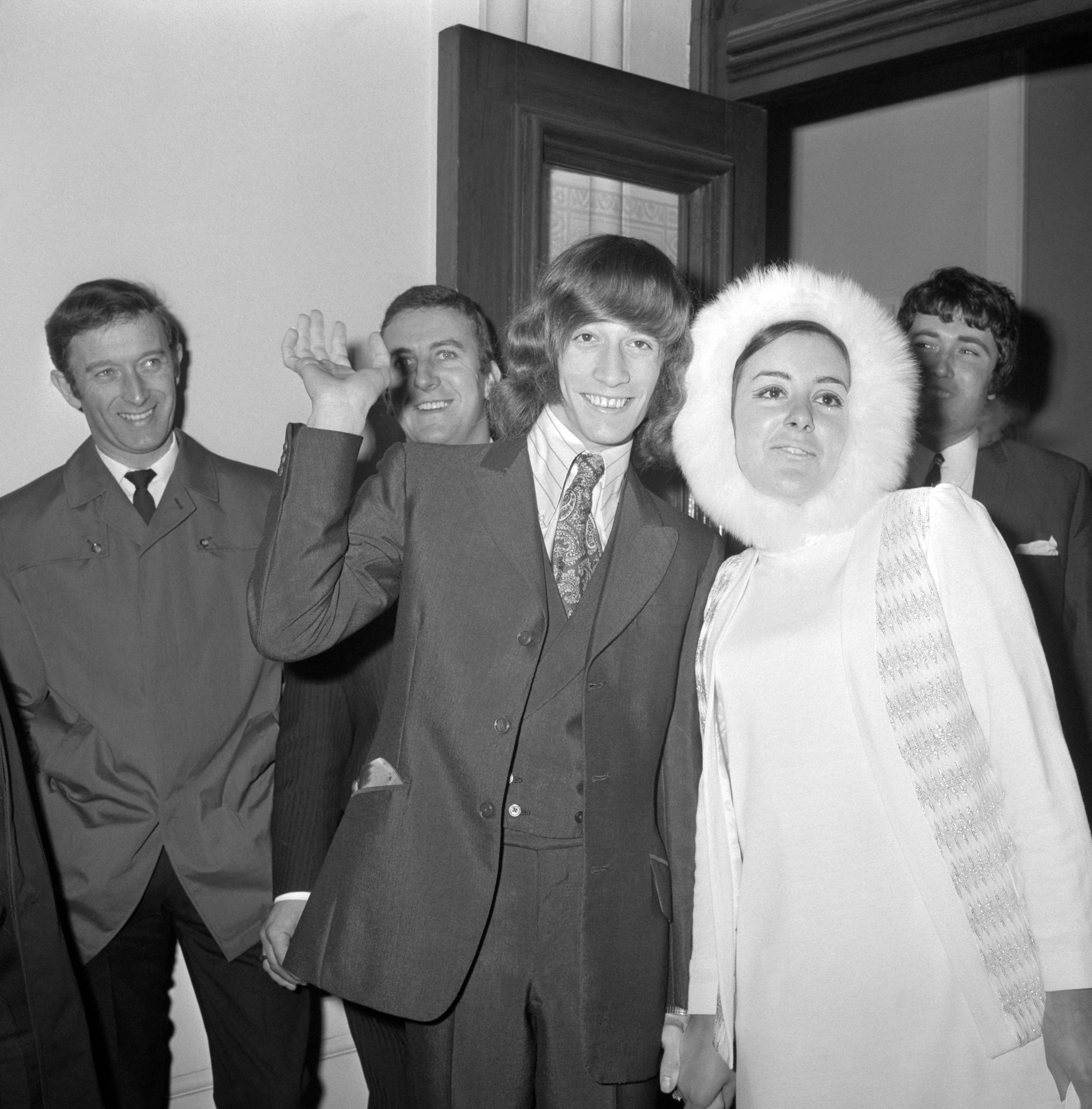 A wave from 19 year old Robin Gibb, member of the Bee Gees, as he leaves Caxton Hall register office, London, with his fur-bonneted bride after their wedding. She was 21 year old Molly Hullis, whom Mr Gibb met two years ago shortly after the Bee Gees came to the UK from Australia. The couple had both survived the Hither Green rail crash, which killed 49 people on 5 November 1967. They divorced in 1980.