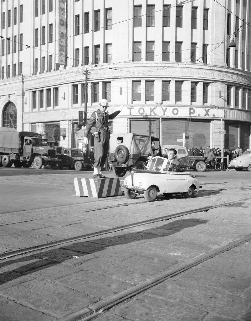 The brainchild of a former kamikaze pilot, this midget auto gets its power from a 30-volt battery. At speeds between 25 and 30 miles per hour, it can travel for six hours before needing recharging. It is priced at about $2,400. It is shown passing the main intersection of the Ginza Street in Tokyo, Dec. 21, 1947. The toy-like car gets a ÂGoÂ signal from Private Jackson Neeley of Hampton, Va., who is attached to the 720th MPs. (AP Photo/Charles Gorry) Ref #: PA.11617099 