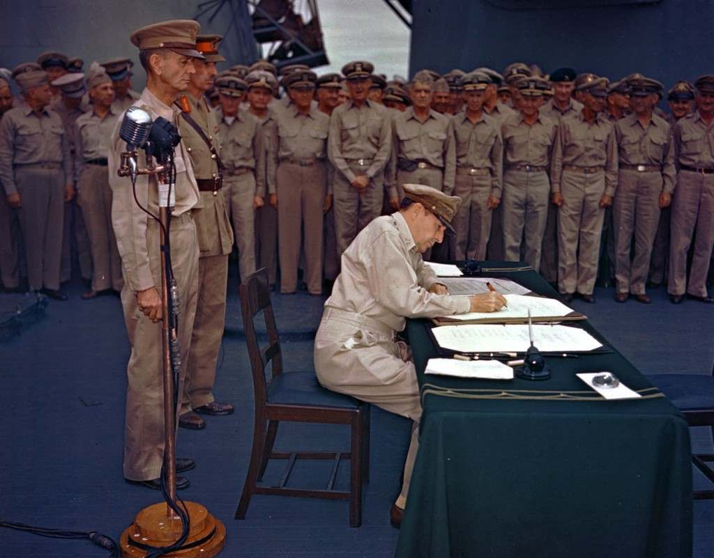 Gen. Douglas MacArthur signs the Japanese surrender documents Sept. 2, 1945, aboard the USS Missouri in Tokyo Bay. Lt. Gen. Jonathan Wainwright, left foreground, who surrendered Bataan to the Japanese, and British Lt. Gen. A. E. Percival, next to Wainwright, who surrendered Singapore, observe the ceremony marking the end of World War II. (AP Photo) Ref #: PA.4762828 