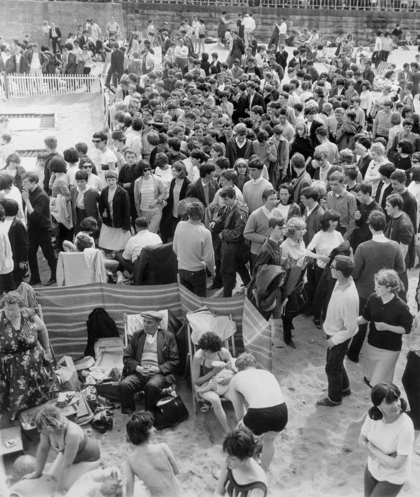 A family shelter behind a windbreak undeterred by the invasion of Mods descending on Margate beach. Mods clashed with Rockers in the second day of violence which saw two youths stabbed. Ref #: PA.5581325  Date: 18/05/1964