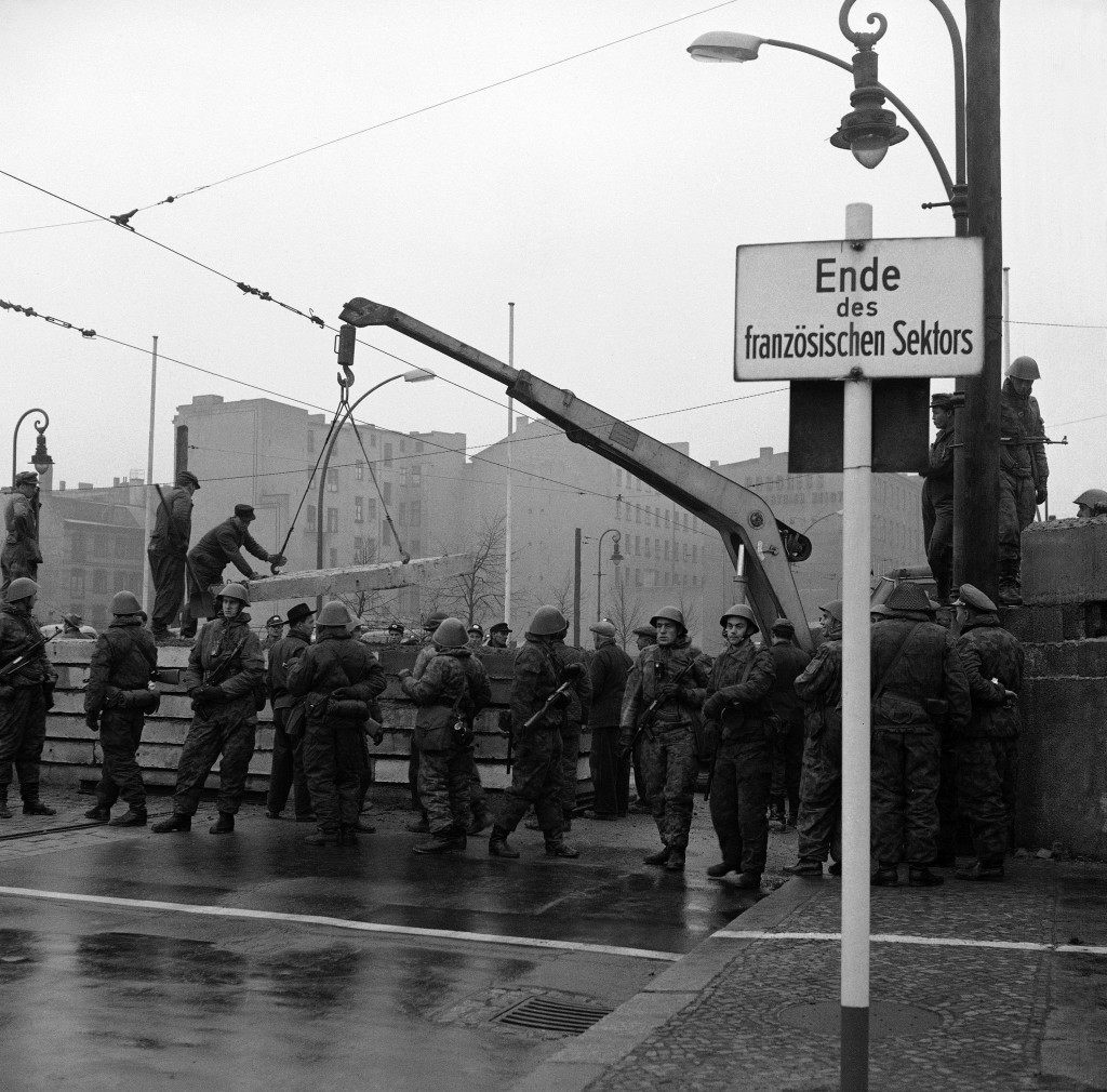 Behind a shield of Communist troops, East German Laborers add to the wall on the East-West Berlin border at the boundary of the French sector in the divided city Dec. 4, 1961. Sign at right marks the border. A crane is used to help workers place a concrete form on the wall near Chausseestrasse. (AP Photo) Behind a shield of Communist troops, East German Laborers add to the wall on the East-West Berlin border at the boundary of the French sector in the divided city Dec. 4, 1961. Sign at right marks the border. A crane is used to help workers place a concrete form on the wall near Chausseestrasse. (AP Photo)