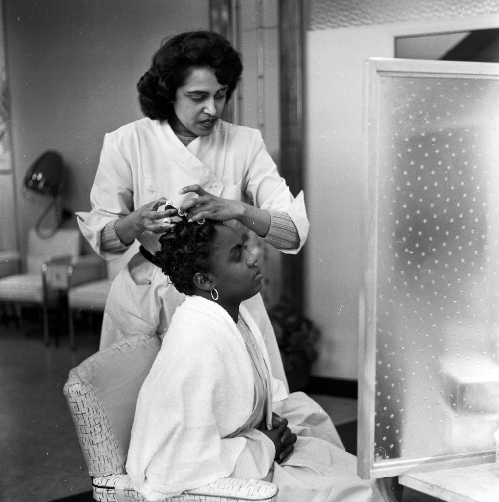 30th April 1957:  A customer has her hair straightened out at pianist Winifred Atwell's hairdressing salon in Brixton, London.  (Photo by Lee Tracey/BIPs/Getty Images)