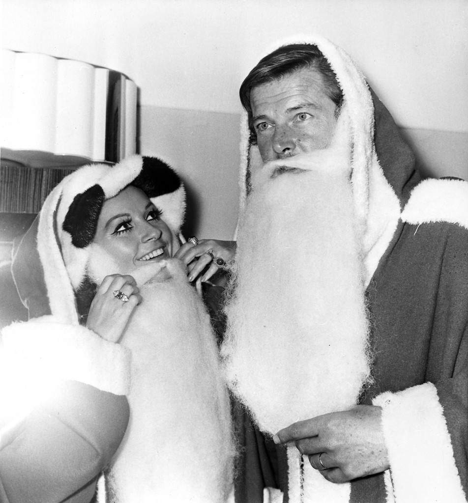 Actors Luisa Mattioli and her husband Roger Moore don "Father Christmas" costumes at the Variety Club of Great Britain's Christmas luncheon at the Savoy Hotel in London, Dec. 9, 1969. They are collecting gifts for sick and deprived children. (AP Photo/Bob Dear) Ref #: PA.4942328 Date: 09/12/1969