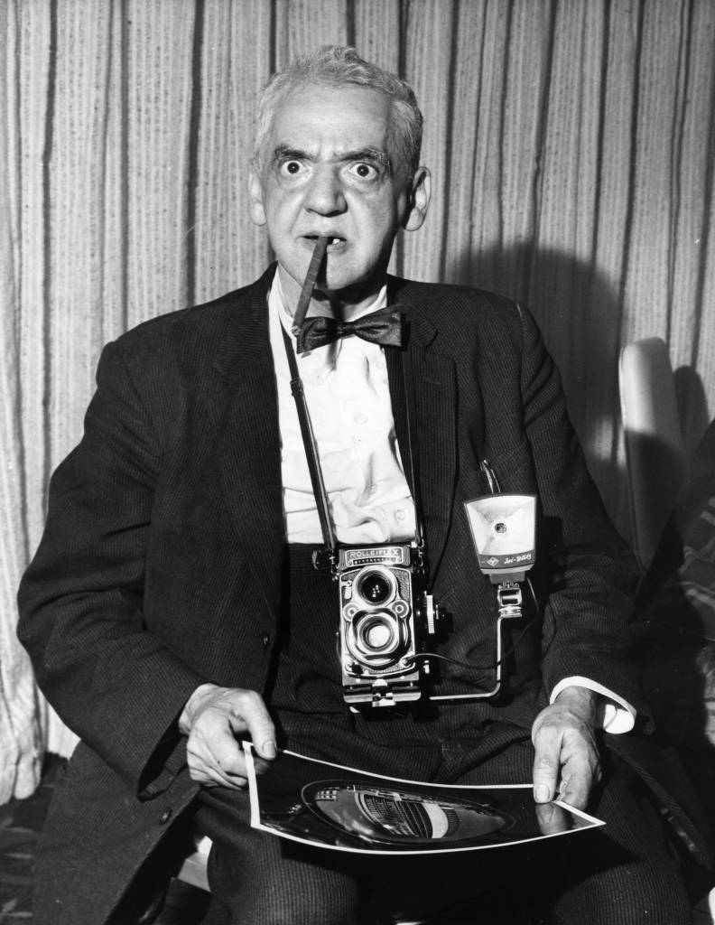 American photographer Weegee (1899 - 1969) with a photograph he took of the newly opened London Hilton Hotel, alongside Hyde Park.
