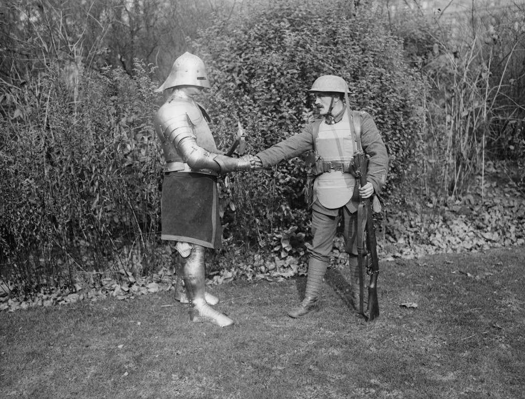 October 1917: A present day soldier armed with a rifle shakes hands with a soldier in a full suit of armour armed with an axe. (Photo by Topical Press Agency/Getty Images)