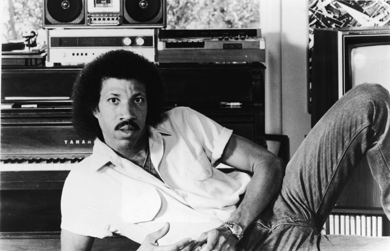 Promotional portrait of American r&b and pop singer Lionel Richie, as he leans on one arm in front of a piano, mid 1980s. (Photo by Hulton Archive/Getty Images)