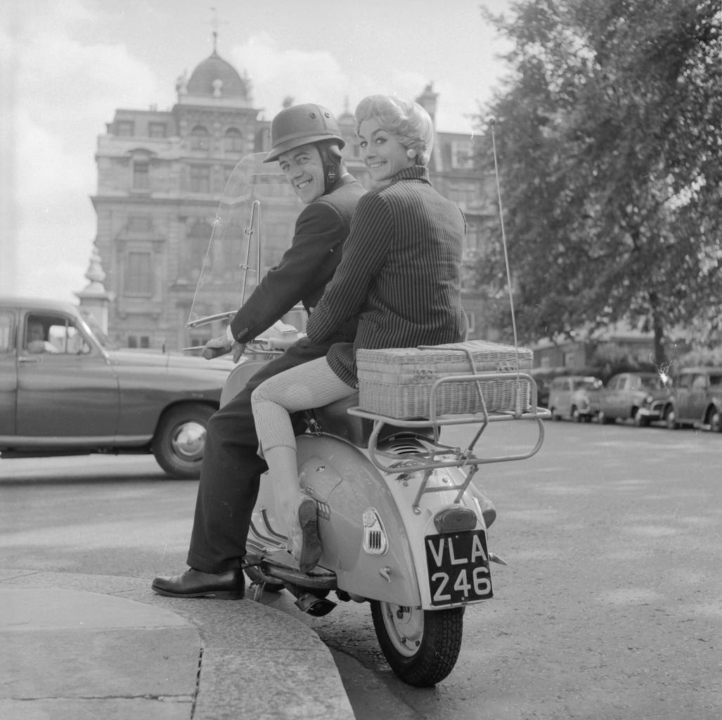 August 1958:  Scooter riders Ron Edney of London and his girlfriend Jean Keyser. Jean is wearing a wig with a specially strengthened base designed by London hairdresser Raymond with the fashion conscious female motorcyclist in mind.  (Photo by Ken Harding/BIPs/Getty Images)