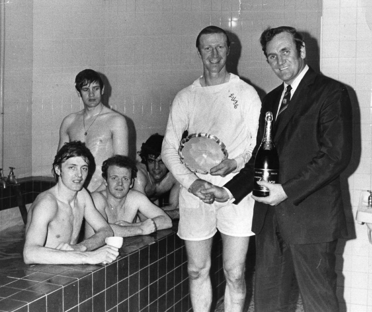 8th April 1972:  Leeds United manager Don Revie presents Jack Charlton with a bottle of champagne and the Footballer of the Month trophy in the changing room after a match. In the bath behind them are fellow Leeds players Clark, Billy Bremner  (1942 -1997), Bates, and Gary Sprake (standing).  (Photo by E. Milsom/Evening Standard/Getty Images)