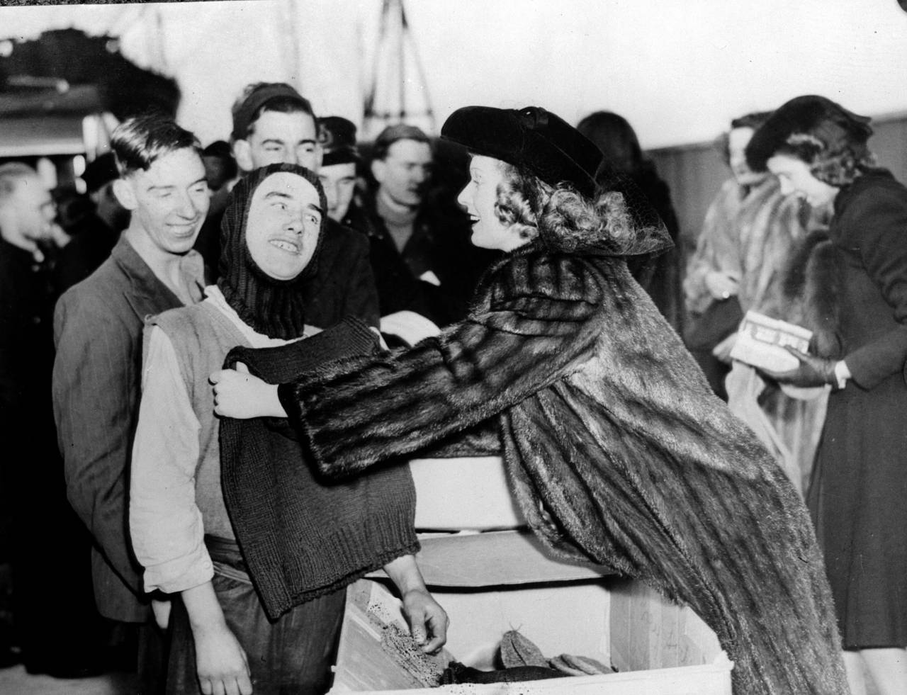 17th January 1941:  British film star Anna Neagle (1904 - 1986) helps a crew member of a British freighter try on a balaclava, gifts from the British War Relief Society of Brooklyn.  (Photo by Fox Photos/Getty Images)