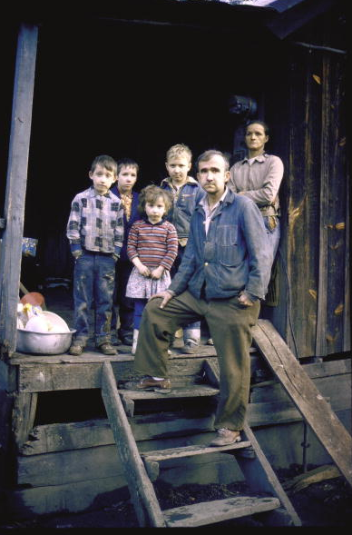 Unemployed miner standing w. his family, who live on Social Security, on porch or their small home re: poverty in Appalachia. 1964