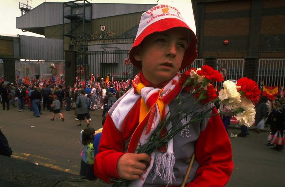1989:  A young unhappy Liverpool supporter carries some flowers in his team's colours to lay in tribute after the Hillsborough disaster at Anfield in Liverpool, England.  Mandatory Credit: Pascal  Rondeau/Allsport
