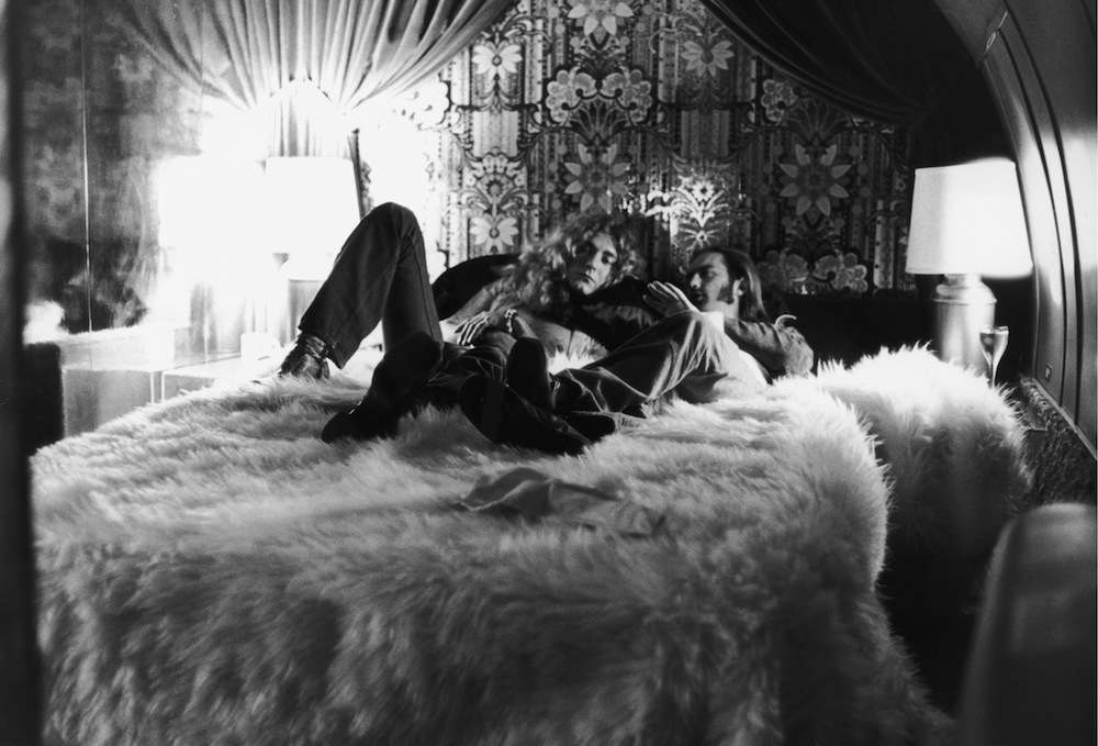 British rock singer Robert Plant (L) of the band Led Zeppelin and the group's road manager, Richard Cole, relax on a bed covered by a fur rug and discuss details of their upcoming concert, New York City, New York, July 30, 1973. (Photo by Express Newspapers/Getty Images)