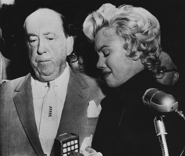 (earful actress Marilyn Monroe w. her lawyer Jerry Giesler clutching her arm as she comes out in front of home to face dozens of reporters after announcement of her divorce fr. baseball great Joe DiMaggio