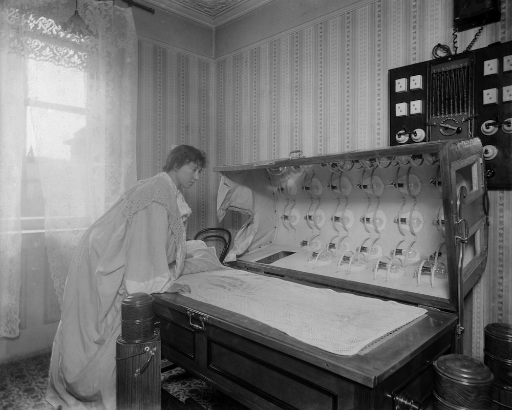 circa 1900: A woman inspects an Electric Bath at the Light Care Institute. The Electric Bath is probably a forerunner of the modern sunbed, although it was more likely used for medicinal reasons. (Photo by Reinhold Thiele/Thiele/Getty Images)