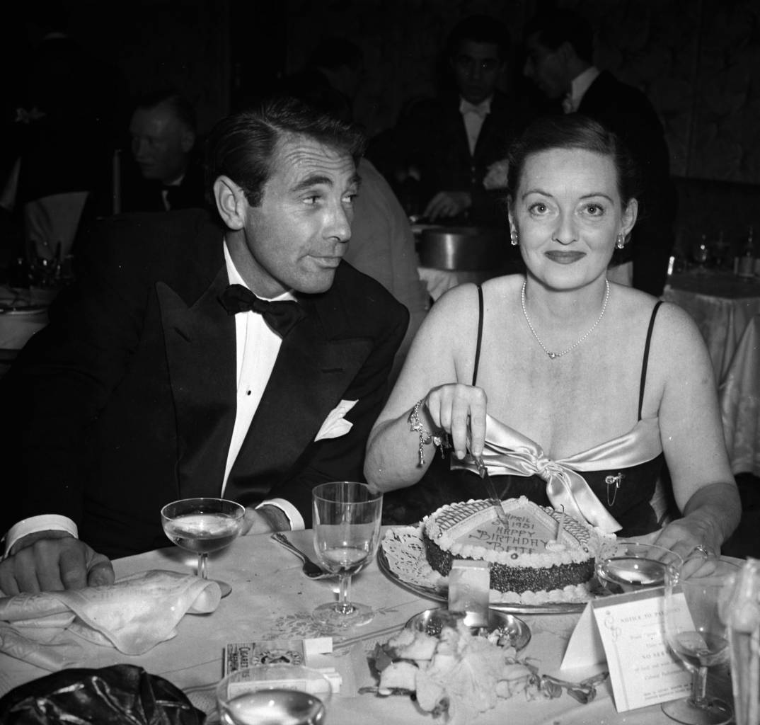 6th April 1951: Film star Bette Davis (1908 - 1989) cutting her birthday cake watched by her actor husband Gary Merrill (1915 - 1990). (Photo by Stanley Sherman/Express/Getty Images)