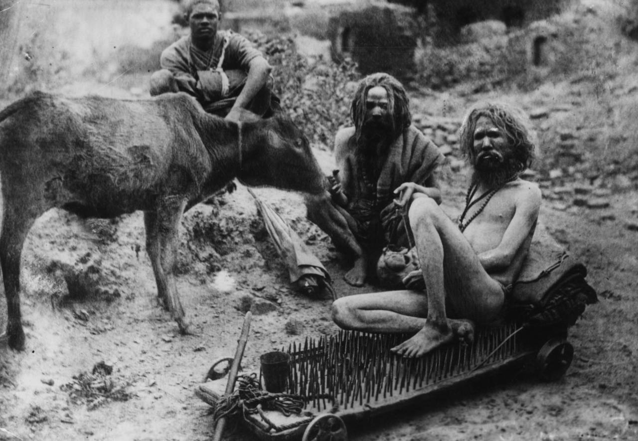circa 1910: A Hindu fakir sitting on a bed of nails with other holy men or sadhu at Benares, a holy place on the river Ganges, India. (Photo by Hulton Archive/Getty Images)
