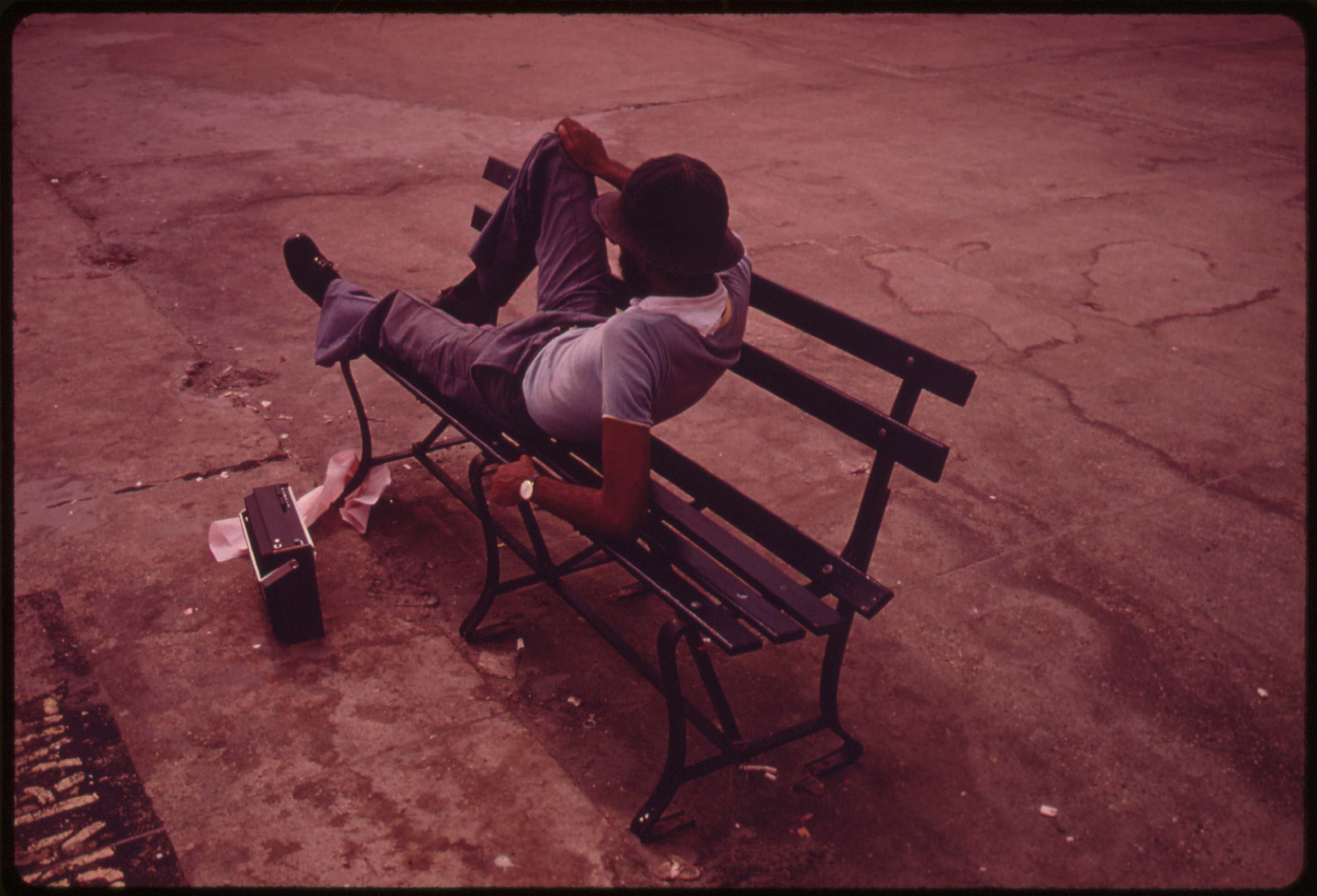 Man lounging on a park bench with his radio on the Reis Park boardwalk in NYC, July 1974.