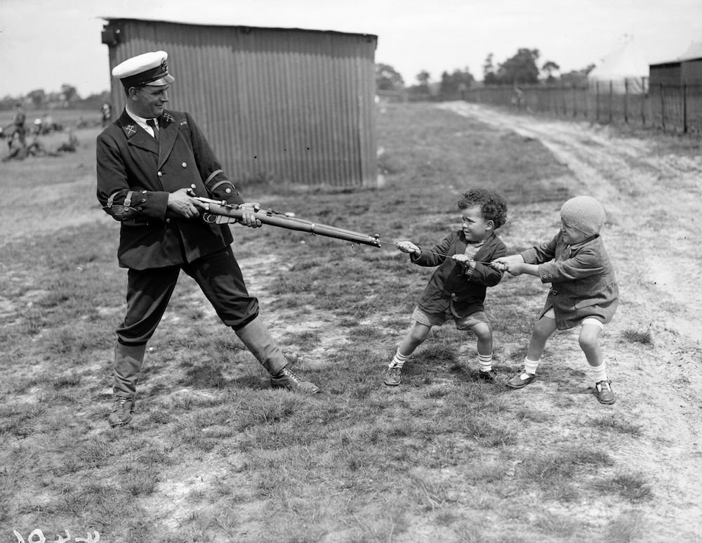 June 1927: Two little boys playing tug of war with a uniformed competitor and his gun during a break in the competition at Bisley rifle range ! (Photo by Fox Photos/Getty Images)