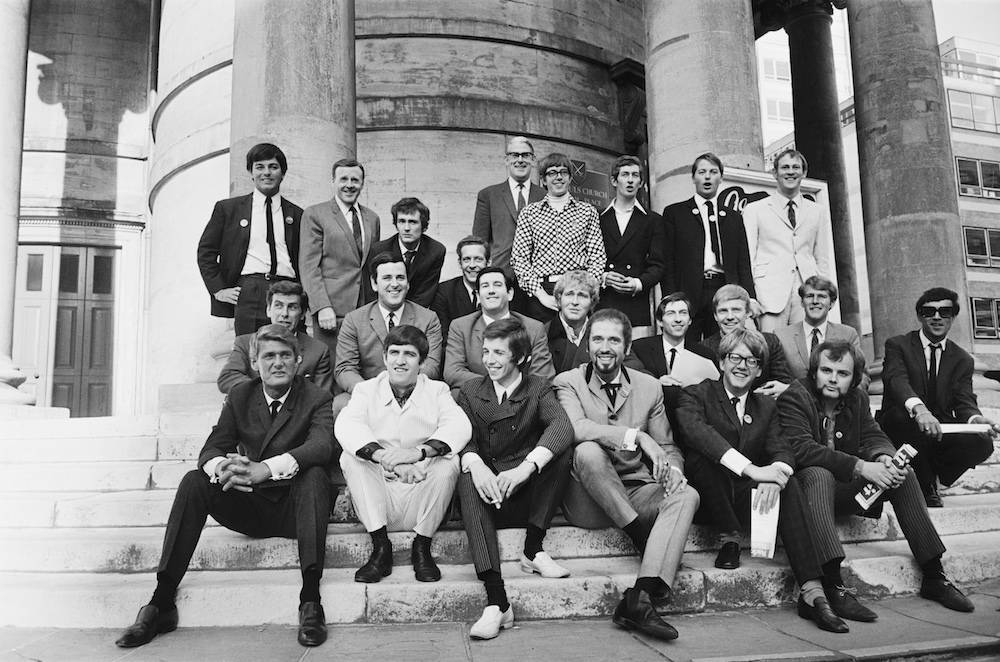 Radio One DJ's pose for a group photograph outside Broadcasting House after the BBC announce their new line up, London, 1967. Back row (left to right); Tony Blackburn, Jimmy Young, Kenny Everett, Duncan Johnson, Robin Scott (controller), David Ryder, Dave Cash, Pete Brady, David Symonds. Middle Row (left to right); Bob Holness, Terry Wogan, Barry Alldiss, Mike Lennox, Keith Skues, Chris Denning, Johnny Moran, Pete Myers. Front row (left to right); Pete Murray, Ed Stewart, Pete Drummond, Mike Raven, Mike Ahern, and John Peel. (Photo by Robert Stiggins/Express/Hulton Archive/Getty Images)