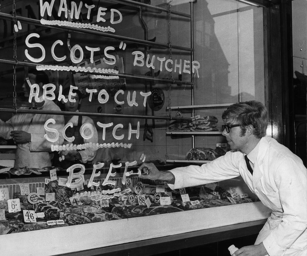 A butcher writes an advert on his shop window, 'Wanted a 'Scots; butcher able to cut 'Scotch' beef'. (Photo by Evening Standard/Getty Images)