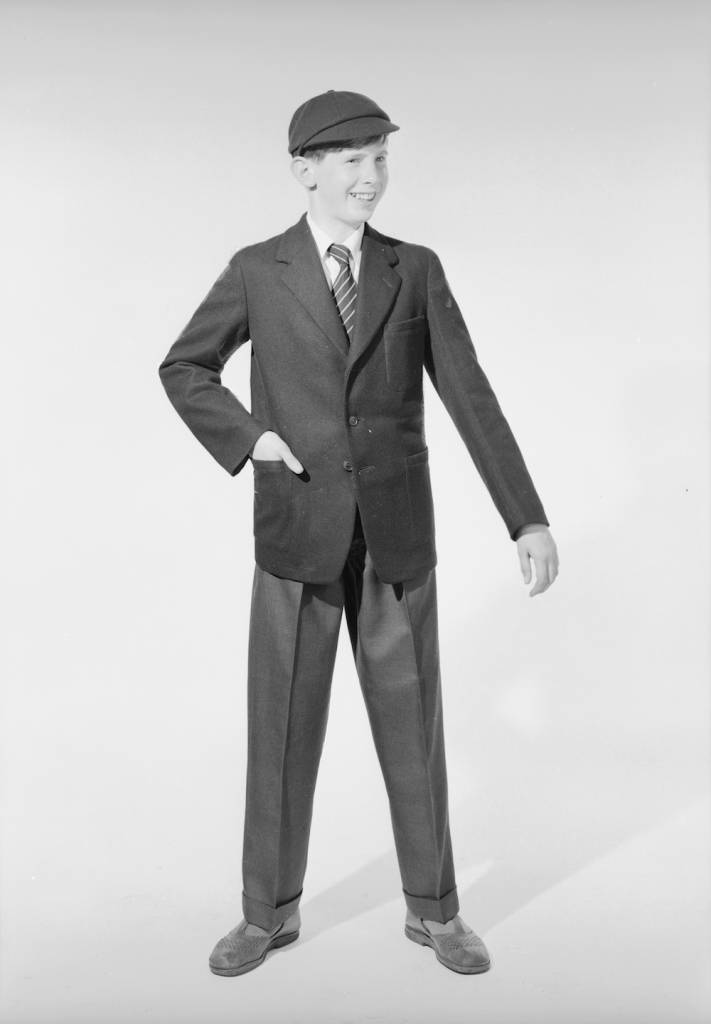 22nd June 1960: A sixties schoolboy modelling stay-press trousers with turn-ups, a jacket and matching peak cap for sale at John Barkers department store in London. (Photo by Chaloner Woods/Getty Images)